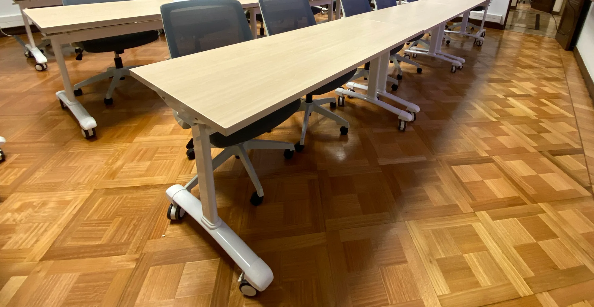 Detalle de mesas, sillas y piso de parquet en una sala de trabajo.