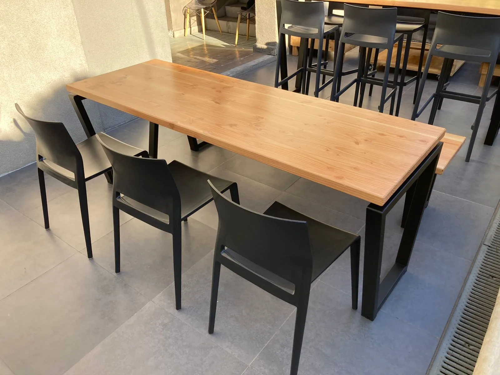 Mesa de madera con sillas negras en una terraza de encuentro.